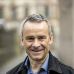 Portraitfoto Sebastian Schmidt, Mann mit blauem Hemd und schwarzer Jeansjacke
