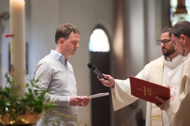 Martin Böing steht vor zwei Priestern und spricht ins Mikrofon