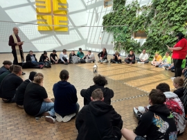 Junge Menschen sitzen im Kreis auf dem Boden, ein Ordensmann steht